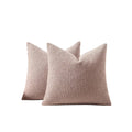Two plush pink pillows on a beige sofa with a white curtain and plant in the background.